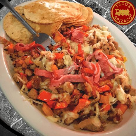 Plato de alambre con pimiento, cebolla y queso fundido, con tortillas al lado.
