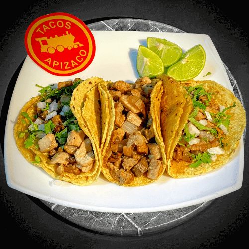 Tres tacos de bistec picado en tortilla de maíz con cilantro y cebolla, y limones en un plato blanco.
