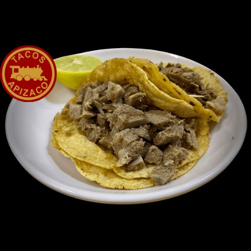 Tacos de lengua en trozos sobre tortilla de maíz, con medio limón en un plato blanco.